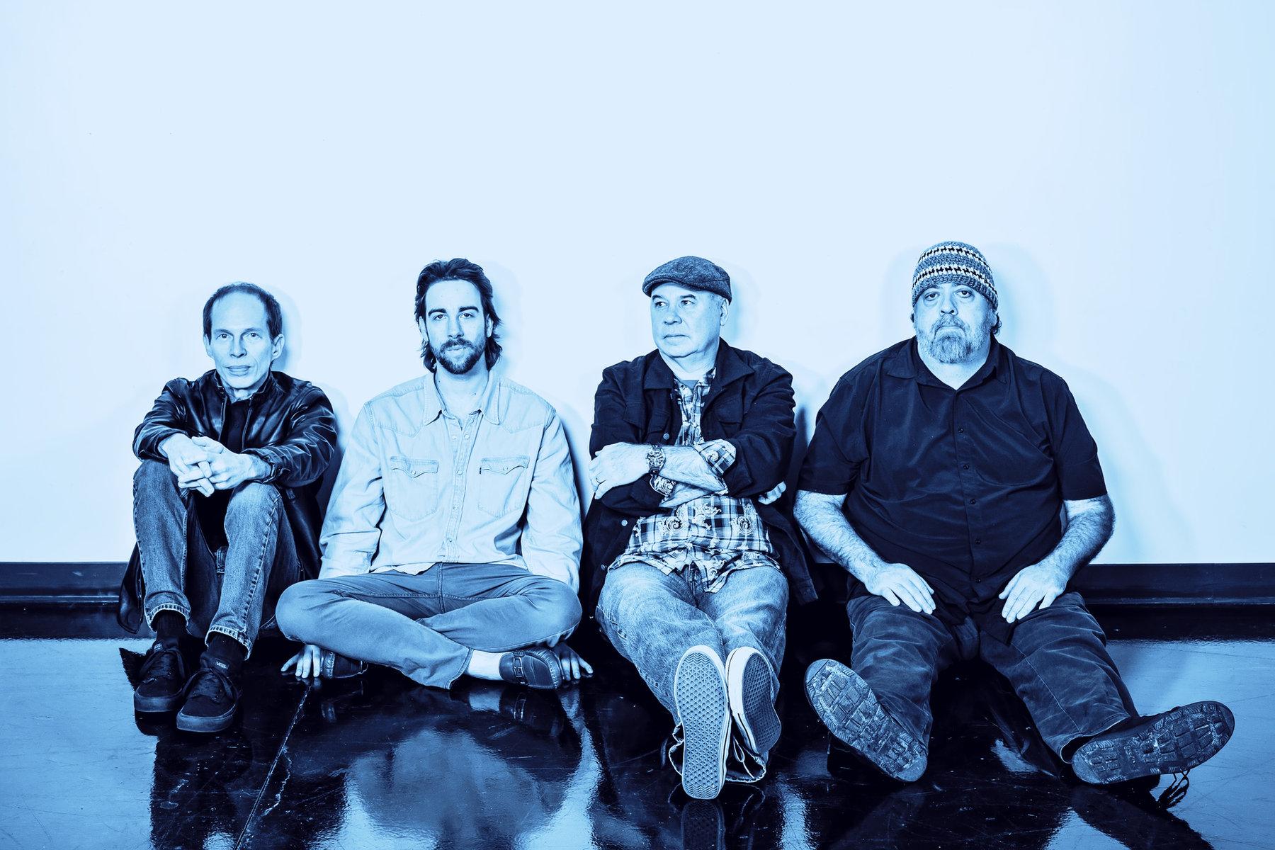Magnum Dopus — four band members sitting against a white wall